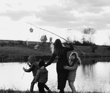 A mother and her children enjoy a serene moment at a lakeshore, captured in black and white.
